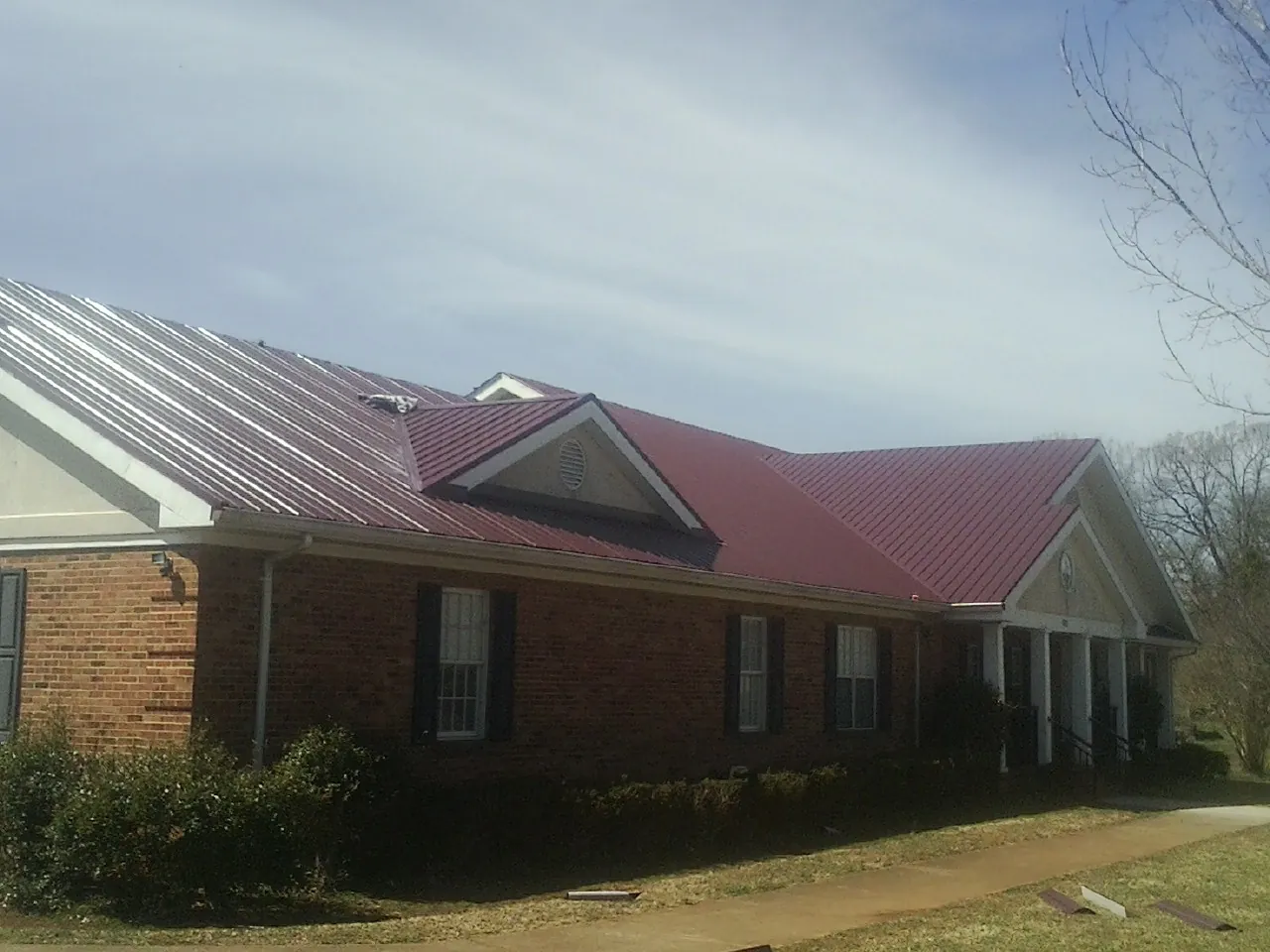 Red metal roof with gabled entries on a long brick building, from a Hail Damage Roof Repair job in Natchez