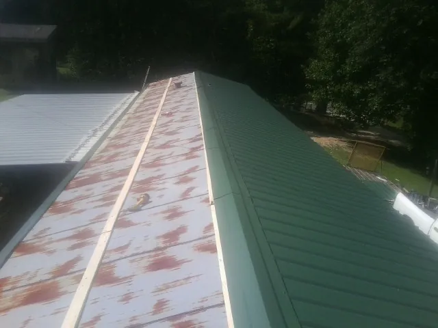 Old rusted panels beside newly installed green metal roofing — Wind Damage Roof Repair by Roofing Brothers in Natchez