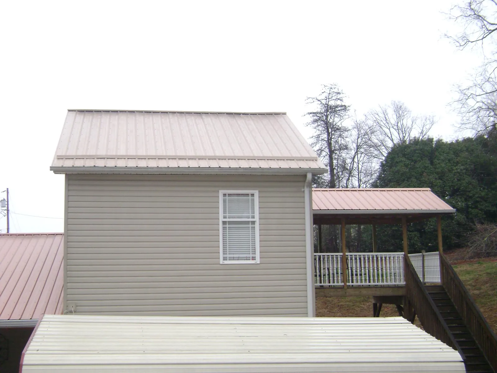 Tan metal roofs on a two story addition and attached porch, from a Roof Replacement job in Natchez